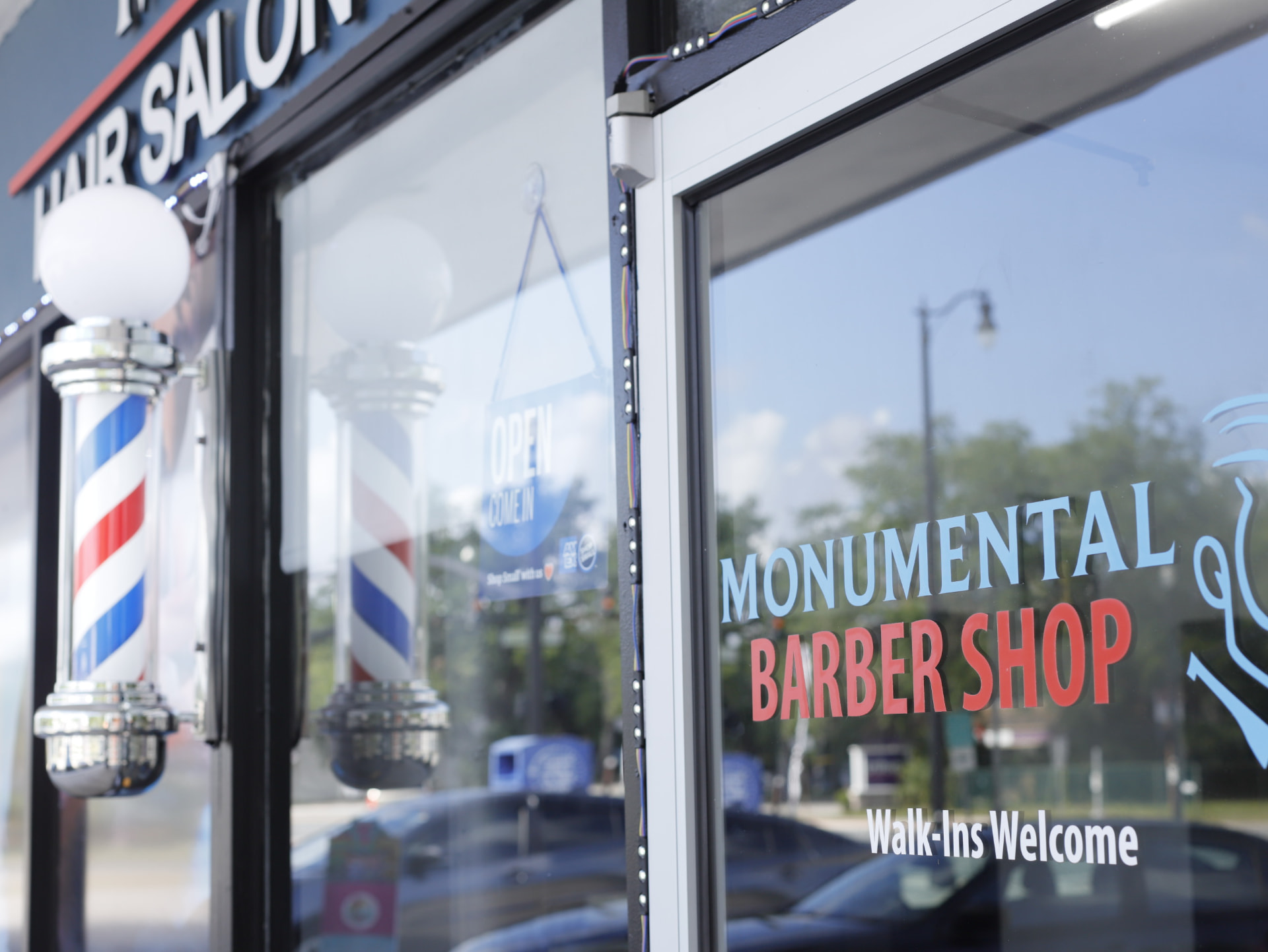 Storefront of Monumental Barber Shop and Hair Salon in Sanford, FL with barber poles and Walk-Ins Welcome signage